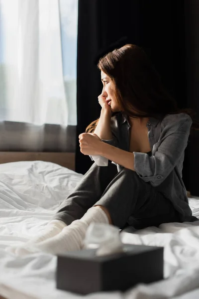 Selektiver Fokus einer depressiven Frau, die in der Nähe einer Gewebebox auf dem Bett sitzt — Stockfoto