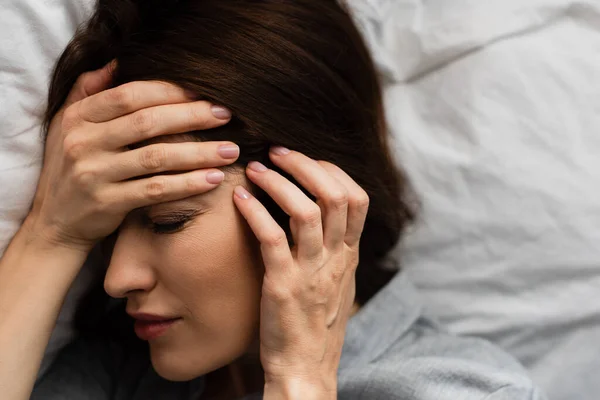 Top view of brunette woman suffering from pain and touching head in bedroom — стоковое фото