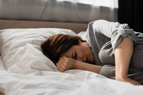 Изнуренная женщина, страдающая от боли и прикосновения к голове, лежа на кровати — стоковое фото