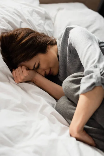 Брюнетка жінка страждає від болю і торкається голови, лежачи на ліжку — стокове фото