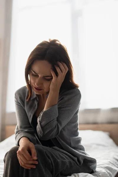 Donna bruna seduta sul letto, che soffre di dolore e tocca la testa a casa — Foto stock