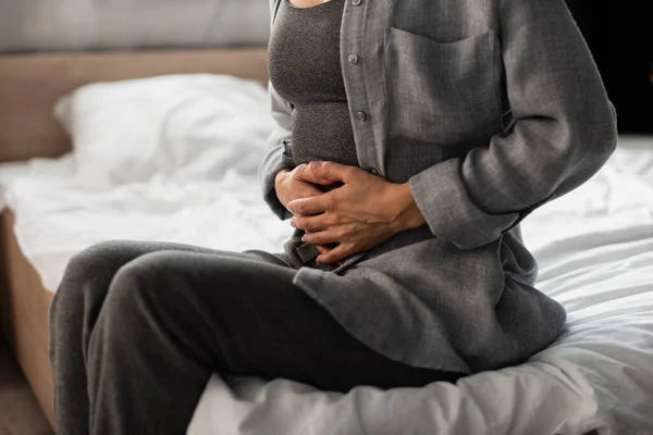 Vista recortada de la mujer que sufre de dolor de estómago en el dormitorio - foto de stock