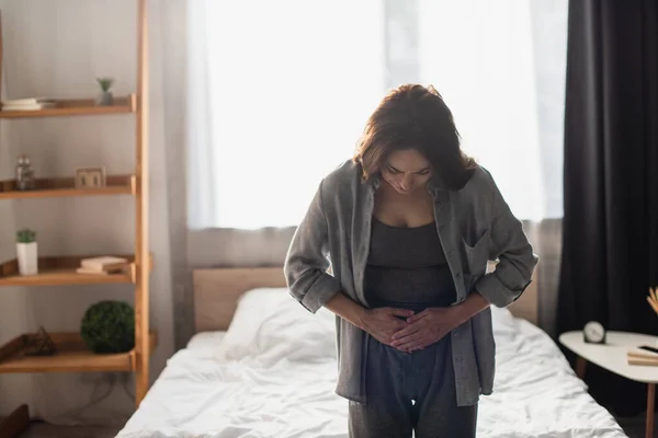Женщина, страдающая от боли в животе в современной спальне — стоковое фото