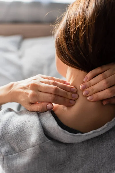 Rückansicht einer brünetten Frau mit Nackenschmerzen im Schlafzimmer — Stockfoto