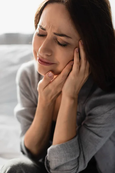 Femme brune avec les yeux fermés touchant le visage tout en souffrant de maux de dents à la maison — Photo de stock