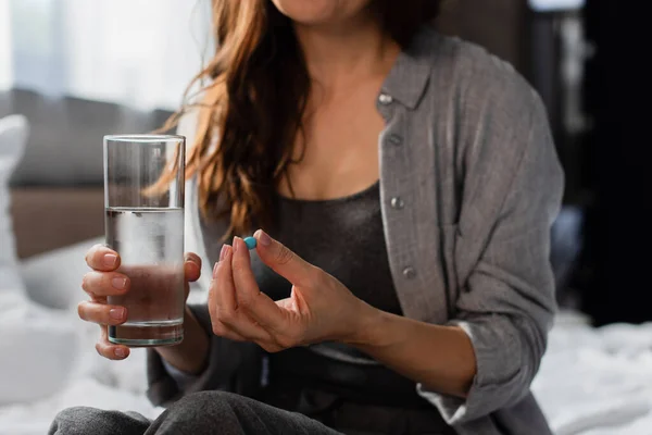 Обрезанный вид брюнетки женщины с таблетками и стаканом воды дома — стоковое фото