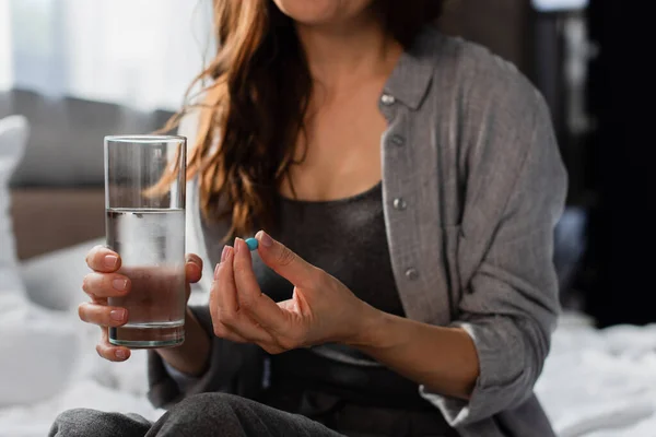 Cropped view of brunette woman holding pill and glass of water at home — Stock Photo