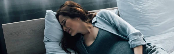 Panorama-Aufnahme einer schwangeren Frau, die unter Schmerzen im Bett leidet — Stockfoto
