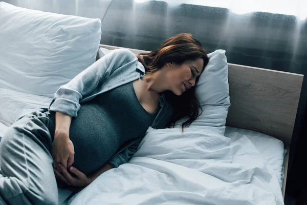 Mulher grávida com olhos fechados que sofre de dor na cama — Fotografia de Stock