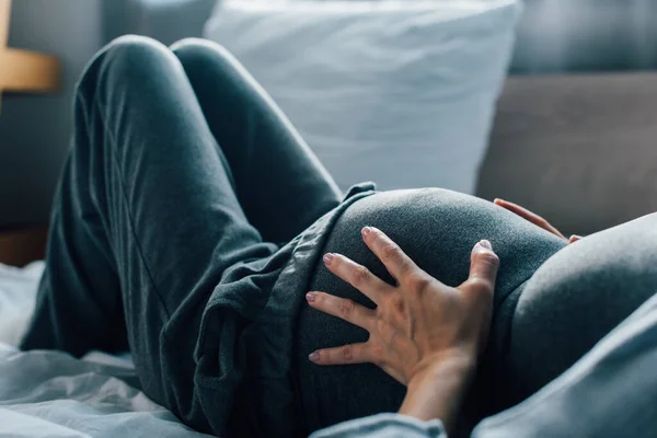 Abgeschnittene Ansicht einer schwangeren Frau, die unter Schmerzen im Schlafzimmer leidet — Stockfoto