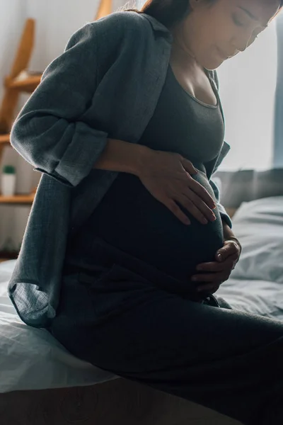 Morena mujer embarazada que sufre de dolor al tocar el vientre en el dormitorio - foto de stock