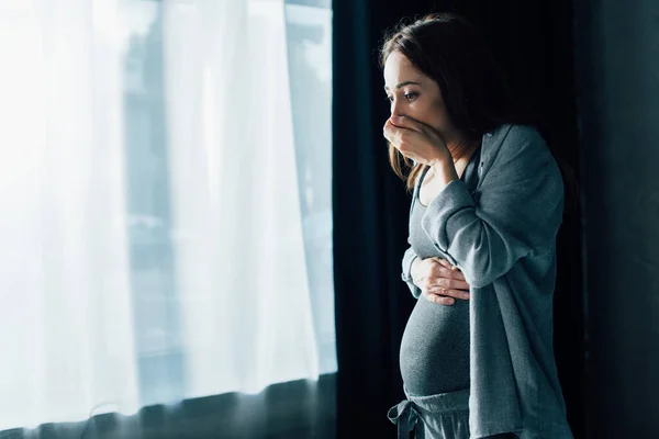 Brunette femme enceinte couvrant la bouche tout en ayant des nausées tout en se tenant à la maison — Photo de stock