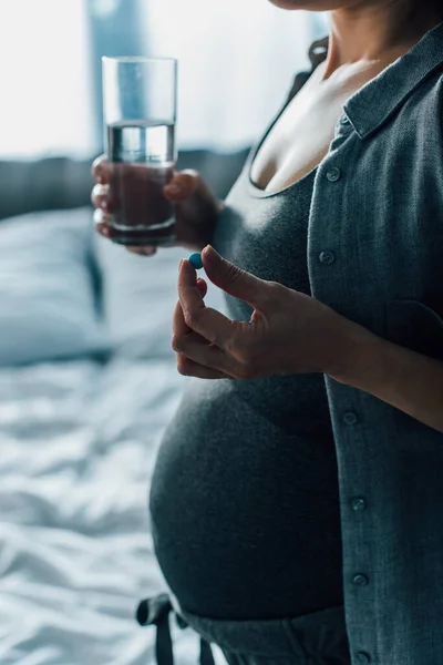 Vue recadrée de la femme enceinte tenant verre d'eau et pilule — Photo de stock