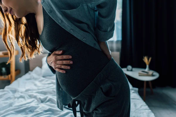 Vista recortada de la mujer embarazada que tiene dolor de espalda en el dormitorio - foto de stock