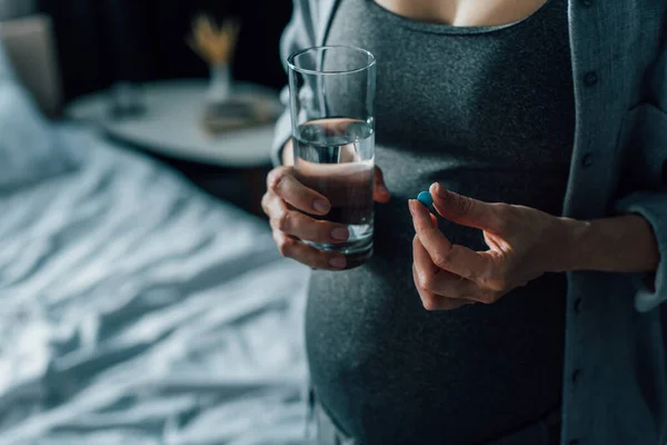Vue partielle de la femme enceinte tenant un verre d'eau et une pilule — Photo de stock