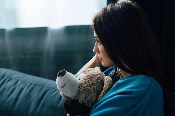 Depressed brunette woman holding teddy bear while looking away — Stock Photo