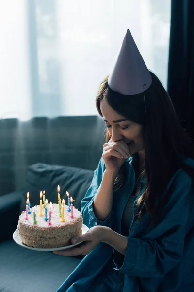 Sad woman in party cap crying and holding birthday cake with candles — Stock Photo