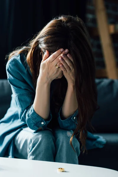 Depressive Frau verdeckt Gesicht, während sie neben Couchtisch mit goldenem Ring sitzt, Scheidungskonzept — Stockfoto