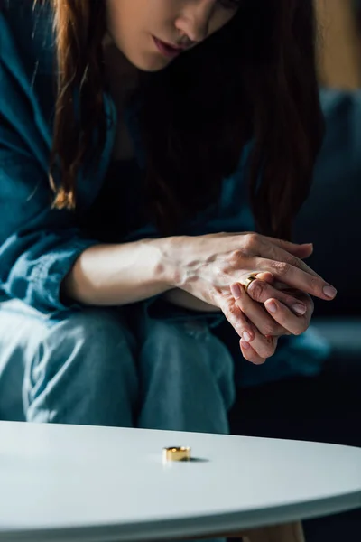 Vue recadrée de la femme brune assise près de la table basse et décollant anneau d'or, concept de divorce — Photo de stock