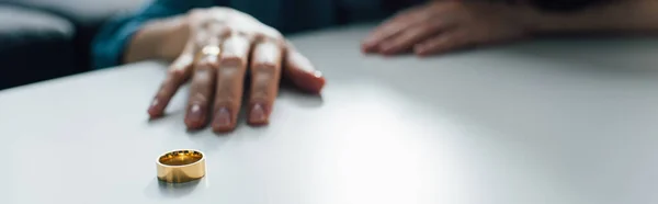 Cosecha panorámica de la mujer que alcanza anillo de oro en la mesa de café, concepto de divorcio - foto de stock