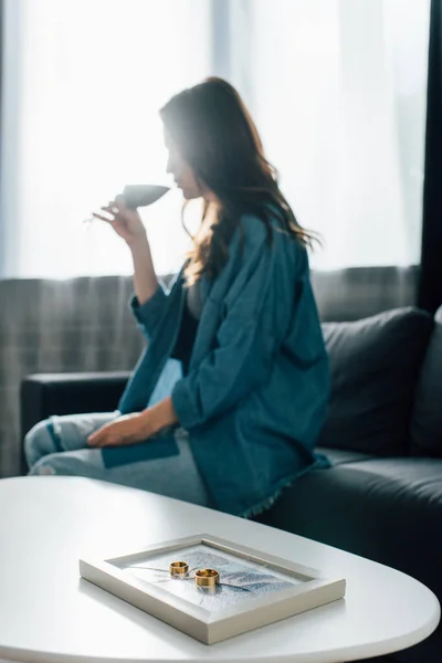 Selective focus of golden rings on photo frame with broken glass near woman drinking wine, divorce concept — Stock Photo