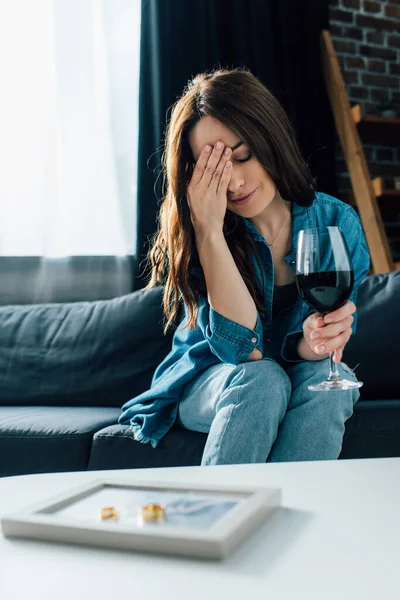 Selective focus of depressed woman with glass of wine near golden rings on photo frame, divorce concept — Stock Photo