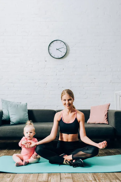 Donna in abbigliamento sportivo seduta in posa yoga vicino figlia sul tappeto fitness — Foto stock