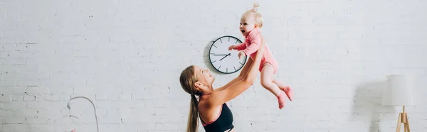 Tiro panorâmico de mulher em sportswear segurando filha infantil em casa — Fotografia de Stock