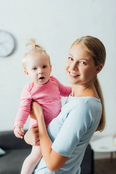 Femme regardant la caméra tout en tenant bébé fille à la maison — Photo de stock