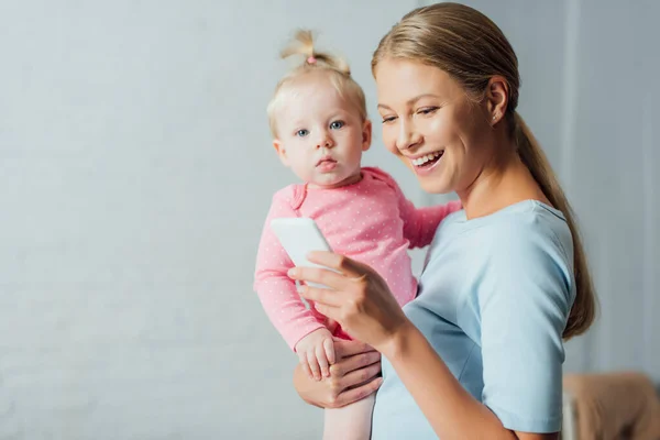 Focus selettivo della donna che utilizza lo smartphone mentre la bambina guarda la fotocamera — Foto stock