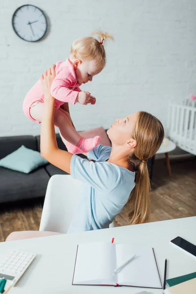 Selektiver Fokus der Mutter, die ihr Baby in der Nähe von Smartphone, Taschenrechner und Schreibwaren auf dem Tisch hält — Stockfoto