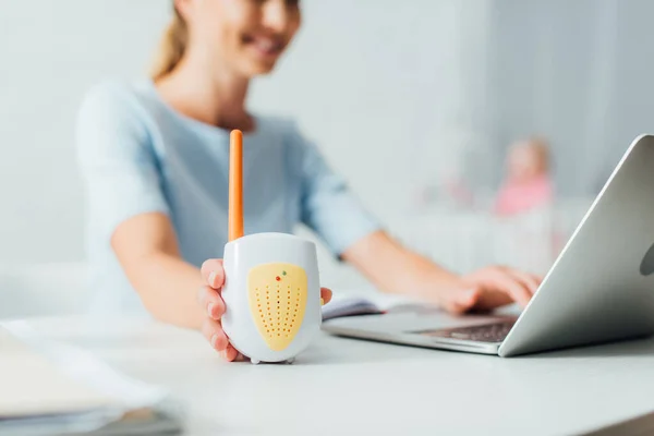Selective focus of woman holding baby monitor while using laptop at table — Stock Photo