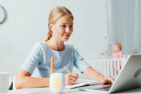 Enfoque selectivo de la mujer que trabaja con el ordenador portátil y portátil cerca del monitor del bebé en la mesa - foto de stock