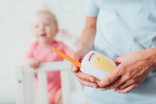 Enfoque selectivo de la madre sosteniendo el monitor del bebé cerca de la hija en segundo plano - foto de stock