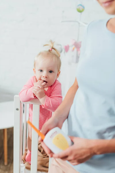 Selective focus of infant in crib near mother holding baby monitor — Stock Photo