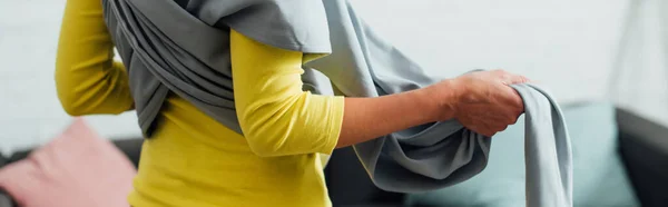 Panoramic shot of woman wearing baby sling in living room — Stock Photo