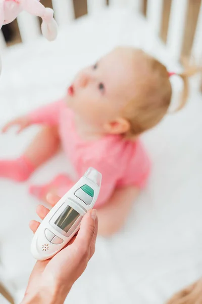 Selektiver Fokus der Mutter, die Inhalator in der Nähe des kleinen Mädchens in der Krippe hält — Stockfoto