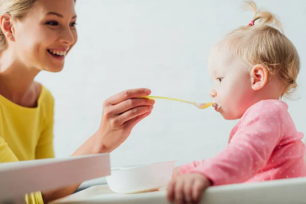 Foco seletivo da mãe alimentando a filha com comida de bebê em casa — Fotografia de Stock