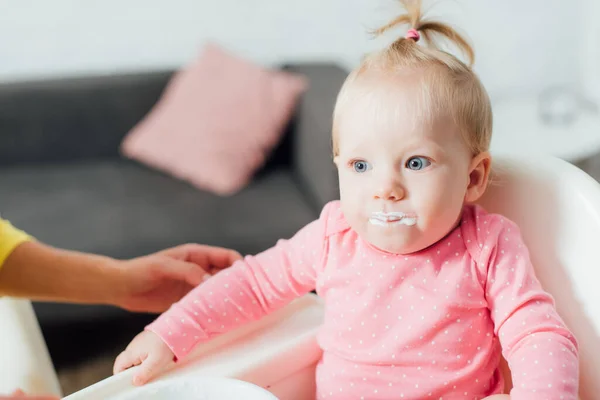 Selective focus of baby girl with messy mouth sitting on feeding chair near mother at home — Stock Photo