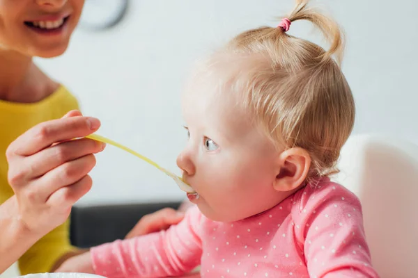 Focus selettivo della donna che alimenta la figlia con cibo per bambini a casa — Foto stock