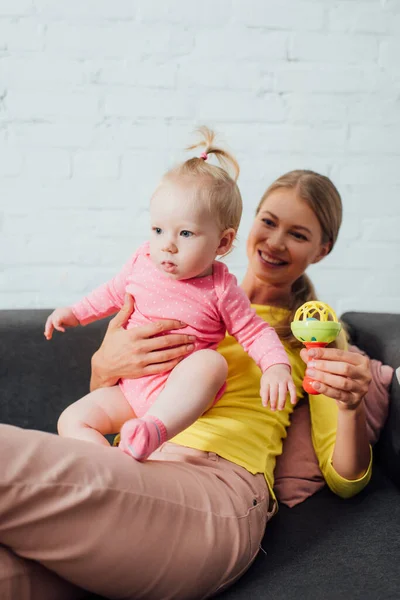 Focus selettivo di donna che tiene giocattolo e figlia neonata sul divano — Foto stock