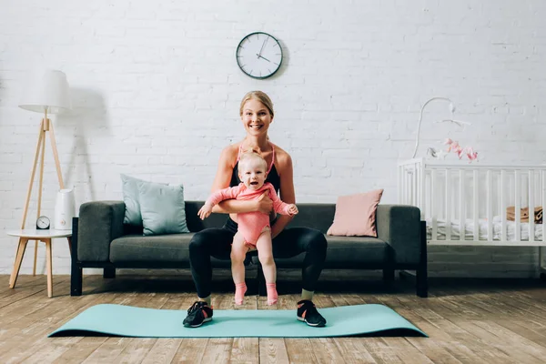 Deportiva abrazando a su hija bebé mientras entrena en la estera de fitness en la sala de estar - foto de stock