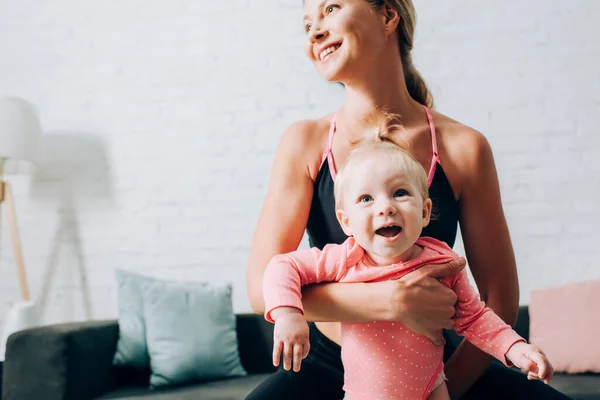 Madre en ropa deportiva sosteniendo bebé niña en casa - foto de stock