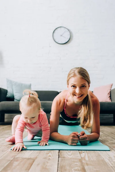 Concentration sélective de la sportive faisant planche près de bébé fille sur tapis de fitness — Photo de stock