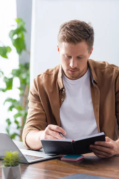 Selektiver Fokus konzentrierter Geschäftsleute, die im Büro neben Laptop auf Notizbuch schauen — Stockfoto