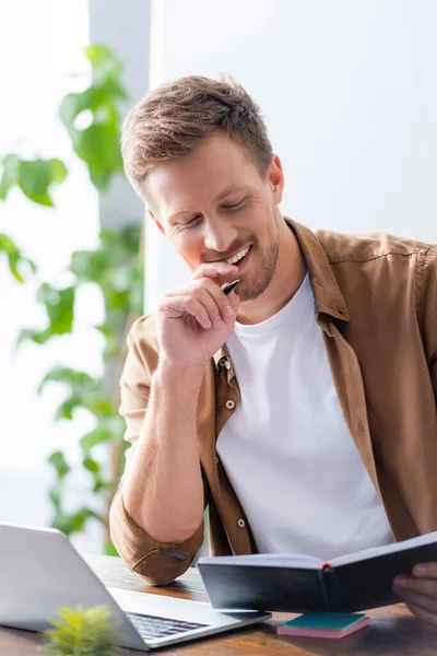 Messa a fuoco selettiva di uomo d'affari guardando notebook mentre seduto sul posto di lavoro vicino al computer portatile — Foto stock