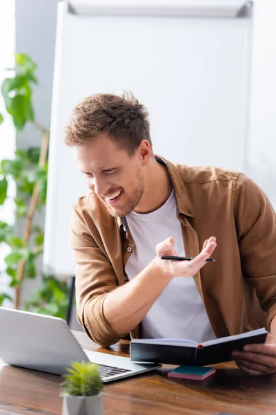 Young businessman holding notebook and pen during video chat on laptop — Stock Photo