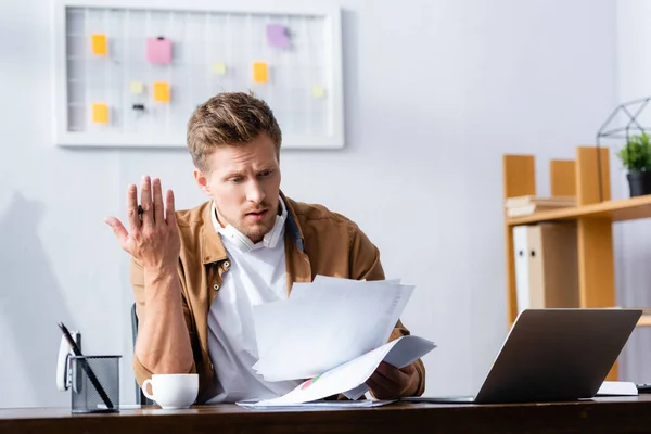 Découragé homme d'affaires avec casque sans fil sur le cou travaillant avec des papiers dans le bureau — Stock Photo