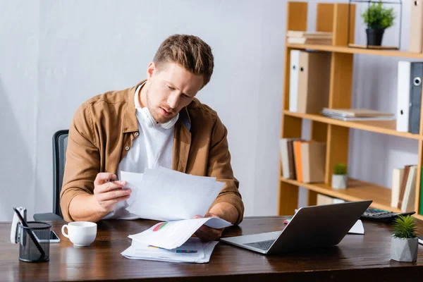 Konzentrierter Geschäftsmann mit drahtlosen Kopfhörern im Nacken, der im Büro mit Dokumenten arbeitet — Stockfoto