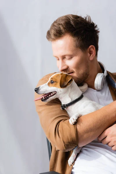Бізнесмен з бездротовими навушниками на шиї приборкаючий джек россел тер'єр собака в офісі — стокове фото